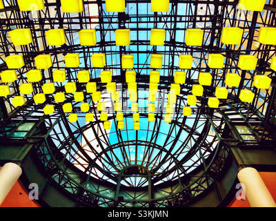 Abgehängte gelbe Lichter von einer hohen Decke mit einem Blick auf den Himmel durch das Glas. Stockfoto