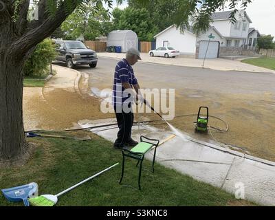 Mann, der im Rahmen einer Frühjahrsreinigung in Utah, USA, einen Bürgersteig mit einem Powerwash absprüht. Stockfoto
