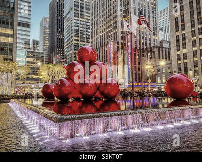 2021 werden riesige Weihnachtsbaumschmuck in einem reflektierenden Pool gegenüber der Radio City Music Hall an einem kalten Feiertagsabend in New York City, USA, stapelt und hell erleuchtet Stockfoto