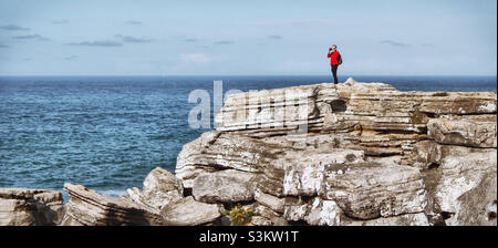 Ein Mann in einem roten Hemd steht auf einem Felsvorsprung, der neben dem Atlantischen Ozean in Peniche, Portugal, Fotos macht Stockfoto