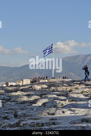 Winterszene auf der Akropolis, Athen, Griechenland, in der Nähe des Parthenons. Besucher sind in einem kleinen Belvedere in der Nähe der griechischen Flagge gruppiert, um die Aussicht zu bewundern. Dahinter steht der Hymettus (1026m), eine Bergkette. Stockfoto