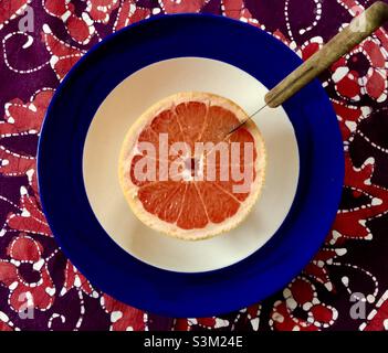 Ein gesundes Frühstück beginnt. Eine Grapefruit mit einem Trennmesser in einer Schüssel auf einer Batik-Tischdecke. Stockfoto