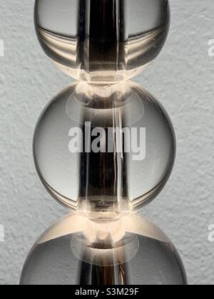 Der Körper einer Lampe aus durchsichtigen Glaskugeln, von unterschiedlicher Größe, die einen Stahlstab bedecken. Mit der aufrechten Lampenfassung ergibt sich eine interessante lineare abstrakte Form. Stockfoto