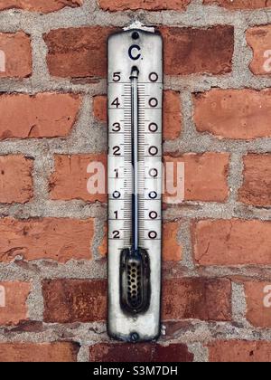 An einer alten roten Ziegelwand hängt ein altes, weiß emailliertes Thermometer mit celsius-Skala und Flüssigkeitssäule Stockfoto
