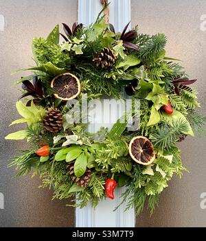 Hausgemachter Weihnachtskranz mit Chilis und Orangen vor der Tür Stockfoto