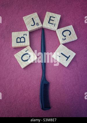 Kleiner Kamm, umgeben von zerkratzbaren Kacheln, bilden das Wortobjekt vor rosa Hintergrund. Stockfoto