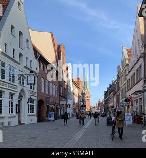 Einkaufen während einer Pandemie: Menschen mit medizinischen Masken im historischen Stadtzentrum von Lüneburg an einem wolkenlosen sonnigen Tag im Winter oder Frühjahr Stockfoto