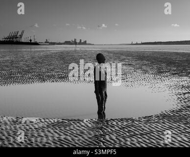 Antony Gormley Statue am Crosby Beach mit der Skyline von Liverpool im Hintergrund. Stockfoto