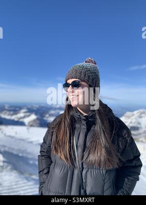 Die junge Frau schaut lächelnd in den Winterferien auf den schneebedeckten Berg in den Uri Alpen, Engelberg, Schweiz Stockfoto