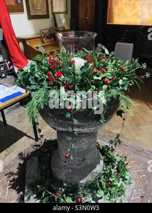 Das mittelalterliche Taufbecken von St Mary’s and All Saints in Dunsfold ist zu Weihnachten geschmückt Stockfoto