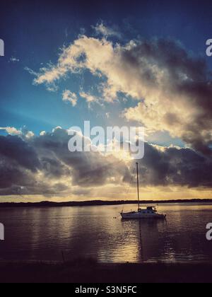 Eine Yacht auf der Pumicestone Passage am frühen Morgen. Das ruhige Wasser reflektiert die Wolken am Himmel. Queensland, Australien. Stockfoto