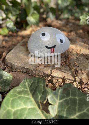 Ein Stein mit einem albernen Gesicht, das darauf gemalt ist, sitzt in einem Garten in angestrahltem Licht. Stockfoto