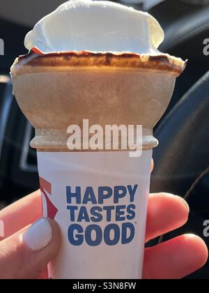 Frau Hand hält Eis-Kegel mit dem Slogan Happy Tastes Good Stockfoto