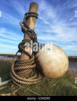 Eine Markierungsboje und ein Seil umwickelt einen Holzpfosten gegen einen blauen Himmel. Stockfoto