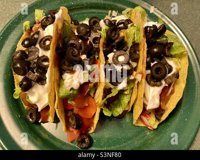 4 Taco-Schalen auf einem grünen Teller gefüllt Huhn, Käse, Salsa, Tomaten, Salat, taco-Sauce, saure Rahm und schwarze Oliven in Scheiben geschnitten. Stockfoto