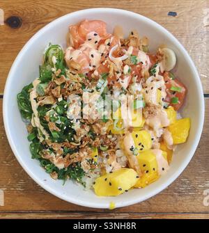 Hawaiianische Schüssel mit Sushi-Reis, Lachs, Mango, Algen, Sriracha-Mayonnaise, Knusprige Zwiebeln, Frühlingszwiebeln und schwarze und weiße Sesamsamen. Stockfoto