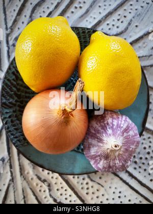 Stillleben von Zitronen, Zwiebeln und Knoblauchzwiebel auf einem Töpferteller Stockfoto