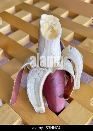 Eine halb gefressene Banane mit roter Haut auf dem Holzgitter eines Couchtisches Stockfoto
