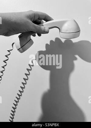 Hand hält einen altmodischen Telefonhörer mit Spiralkabel und Wandschatten. Stockfoto