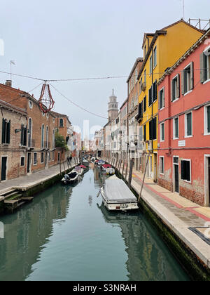 Ruhige Wohngegend in Venedig, Italien. Geparkte Boote auf einem Kanal, umgeben von bunten Häusern und historischen Apartmentgebäuden. Stockfoto