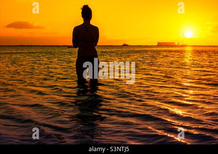Eine Dame, die einen wunderschönen Sonnenuntergang mit Sonnenuntergangshintergrund im Ala Moana Beach Park in Honolulu City Oahu Island Hawaii beobachtet Stockfoto