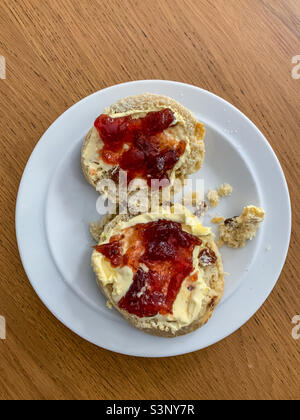 Fruchtkegel mit gerinnter Creme und Erdbeermarmelade auf weißem Teller Stockfoto