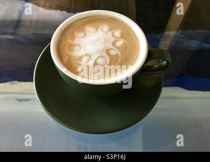 Coffee Latte mit schöner Schaumstoffverzierung in einer grünen Tasse auf einem bunten Glastisch Stockfoto