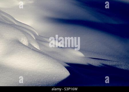 Elegante Schneeformation im Sonnenlicht mit funkelnden Schneekristallen und bläulichen Schatten Stockfoto