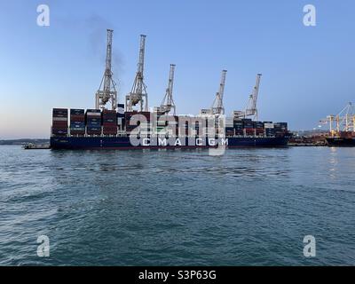 Großes Containerschiff CMA CGM voll beladen im Hafen von Koper, Slowenien, vertäut. Hinter dem Schiff befinden sich Portalkrane in vertikaler Position, die für den Be- und Entladebetrieb bereit sind. Stockfoto