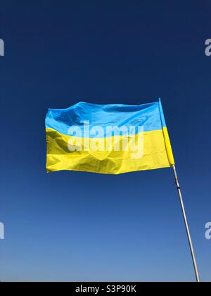 Die ukrainische Flagge wurde im starken Wind gegen einen blauen Himmel ausgestreckt Stockfoto