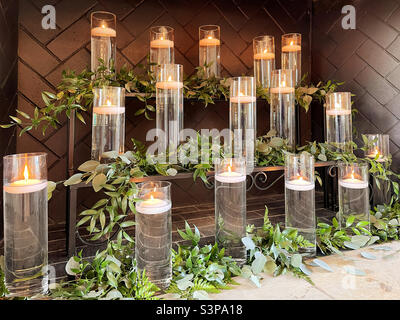 Mit Wasser gefüllte Glasbehälter mit brennenden Kerzen und Grün in einem Kamin im Innenbereich Stockfoto