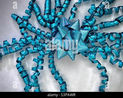 Ein türkisfarbener Geschenkbogen und baumelnde gewellte Bänder, die von oben auf weißem Hintergrund fotografiert wurden. Stockfoto