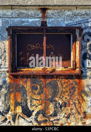 Rostende Metallfensterrahmen auf verlassenen und Graffiti verdeckten Gebäude Stockfoto