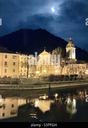 Ein wolkiger Vollmond über der Kirche des heiligen Antonius Abbott, Chiesa Parrocchiale di Sant'Antonio Abate in Dolceacqua, Italien. Stockfoto