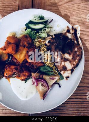 Indian Takeaway Feast - Hühnchen-Dopiaza-Curry, Fleisch-Samosa, Pilzpilz-Pilau-Reis, Peshwari-Naan-Brot, Salat und Minzjoghurt. Stockfoto