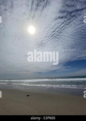 Die Sonne scheint durch die Wolken, während kleine Wellen am Pazifik am Ventura Beach, Kalifornien, brechen. Gleitschirm sichtbar und Inseln in der Ferne Stockfoto
