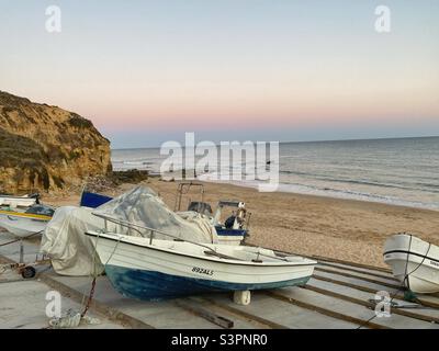 Blick auf das Meer bei Sonnenuntergang mit Booten, die an einem Strand in Olhos de Agua, Algarve, Portugal, geparkt sind. Stockfoto