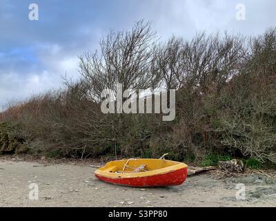 Rot-gelbes Schlauchboot, das auf den Strand gespült wurde Stockfoto