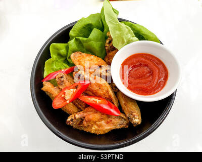 Gebratene Hähnchenflügel in einer Schüssel mit Salat und Chilis mit einer Schüssel würziger Dip-Sauce serviert. Stockfoto