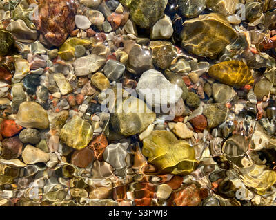 Hintergrund von farbigen Flusssteinen oder Kieselsteinen unter Wasser. Draufsicht. Sauberes und klares Wasser Stockfoto