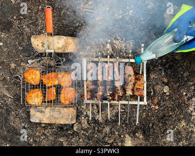 Braten Schweinshauch-Kebab und Hühnershisch-Kebab in der Natur. Schweinebraten auf Spieße und Hähnchenbraten auf einem Grill auf einer offenen Feuerflamme Stockfoto