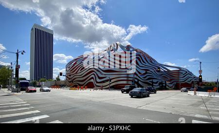LOS ANGELES, CA, APR 2021: Petersen Automotive Museum mit Verkehr, der an einer Kreuzung im Vordergrund vorbeifährt, blauem Himmel mit weißen Wolken über dem Museum Stockfoto