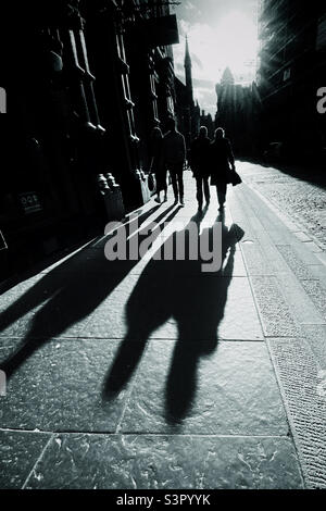 Menschen, die entlang der Royal Mile in Edinburgh spazieren, werden von der späten Nachmittagssonne beleuchtet und werfen lange Schatten Stockfoto