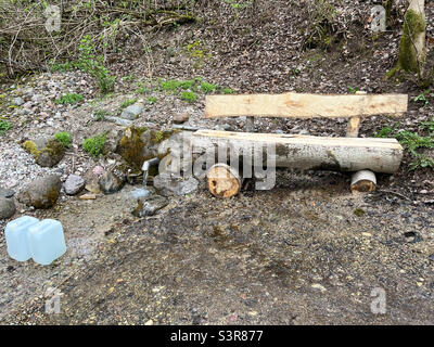 Ein frischer und kühler Frühling kommt aus dem Boden. Kühles und leckeres Quellwasser. Natürliche Grundwasserquelle mit Copyspace. Sitzbank zur Ruhepause Stockfoto