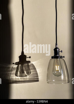 Hängeleuchte mit Glasschirm, LED-Lampe und Schatten an der Wand. Stockfoto