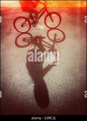 Ein Retro-Film-Effekt-Bild eines Mädchens, das in der späten Nachmittagssonne auf dem Fahrrad reitet. Ein interessanter Schatten? Foto ©️ COLIN HOSKINS. Stockfoto