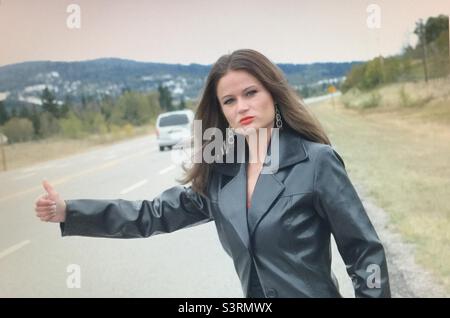 Hitch Wanderer, Frau, hübsches Mädchen, Windy day, brünette, Ein Ritt, Daumen hoch, fließendes Haar, Straße, braucht eine Fahrt Stockfoto