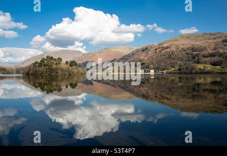 Eine malerische und malerische Landschaft des Grassmere Sees in Ambleside im Lake District National Park mit flauschigen weißen Wolken, die sich in den ruhigen Gewässern und Bergen und Hügeln im Hintergrund widerspiegeln Stockfoto