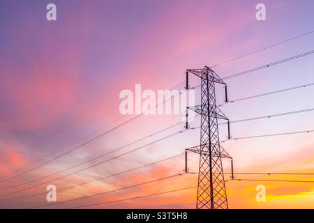 Blick in den niedrigen Winkel auf einen hohen Strompylon, der Hochspannung durch Kabel transportiert, mit farbenprächtiger Sicht bei Sonnenuntergang und Kopierraum Stockfoto