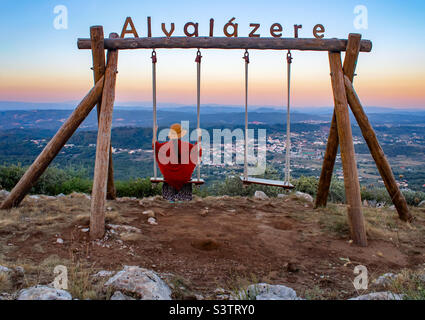 Eine Frau in einem Sommerhut und einer leichten Umhüllung genießt den Sommerabend mit Blick über Alvaiazere von einer Schaukel hoch über der Stadt Stockfoto